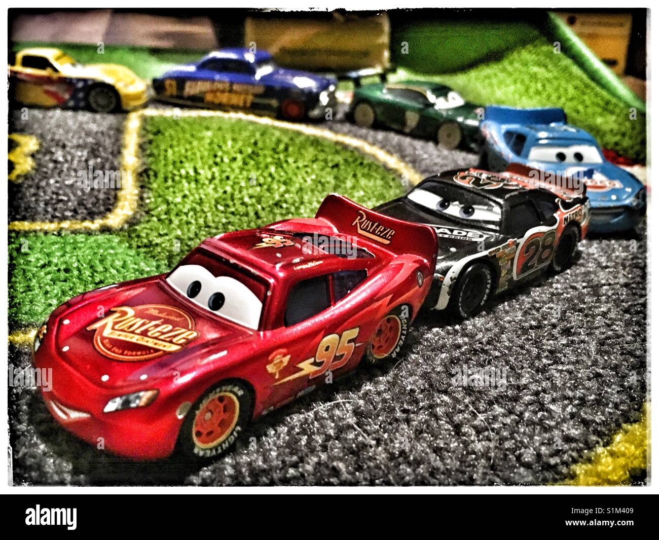 Lighting McQueen conduce altri toy cars racing su un bambino di gara mat. Foto Stock