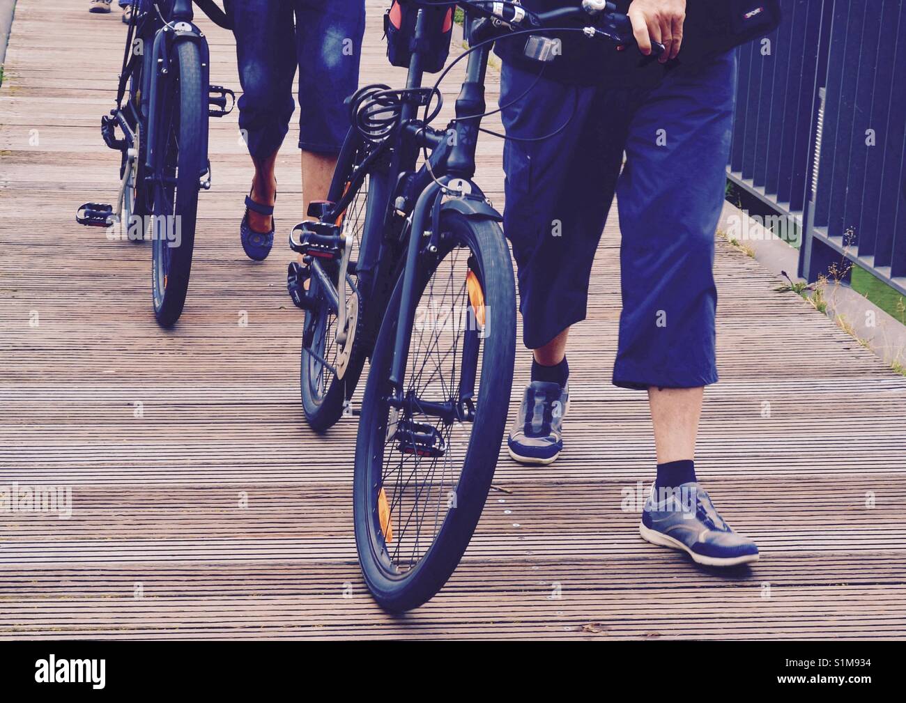 Primo piano di due persone a piedi biciclette su decking in legno. Vista  frontale che mostra la gente gambe e spingere solo bici Foto stock - Alamy