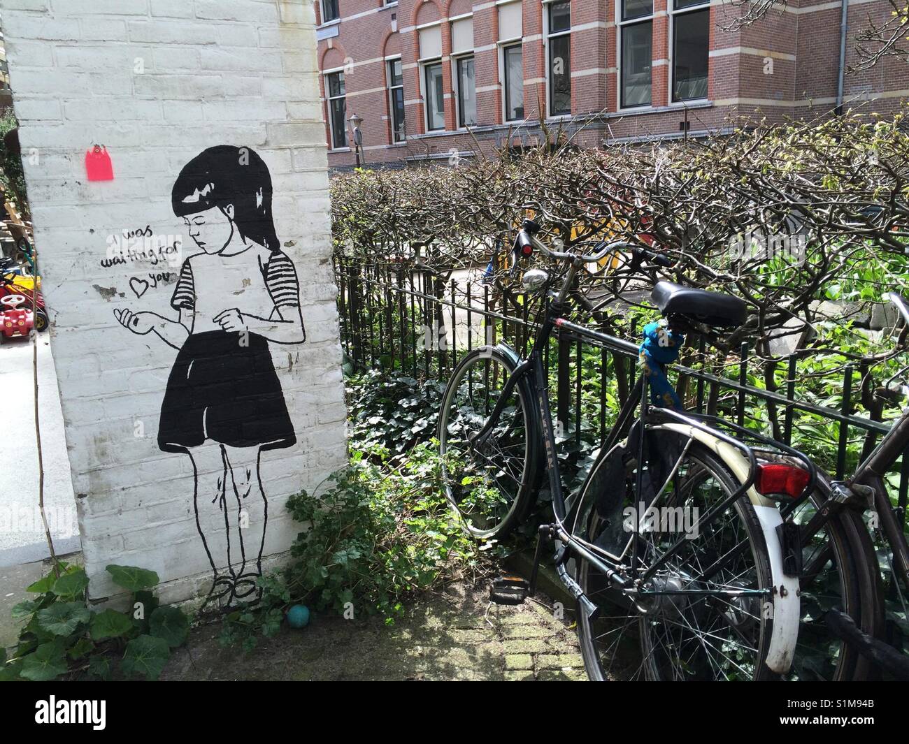Amsterdam Graffiti in strada mostra ragazza, accanto a una bici in giardino, Strassenszene mit Vorgarten und Fahrrad, Radlstadt Foto Stock