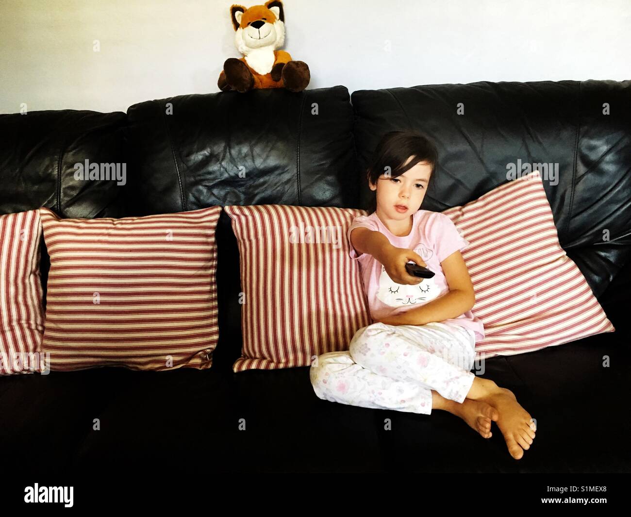 Ragazza su un divano cambiare i canali sul televisore con telecomando - Immagine stock catturata con smartphone