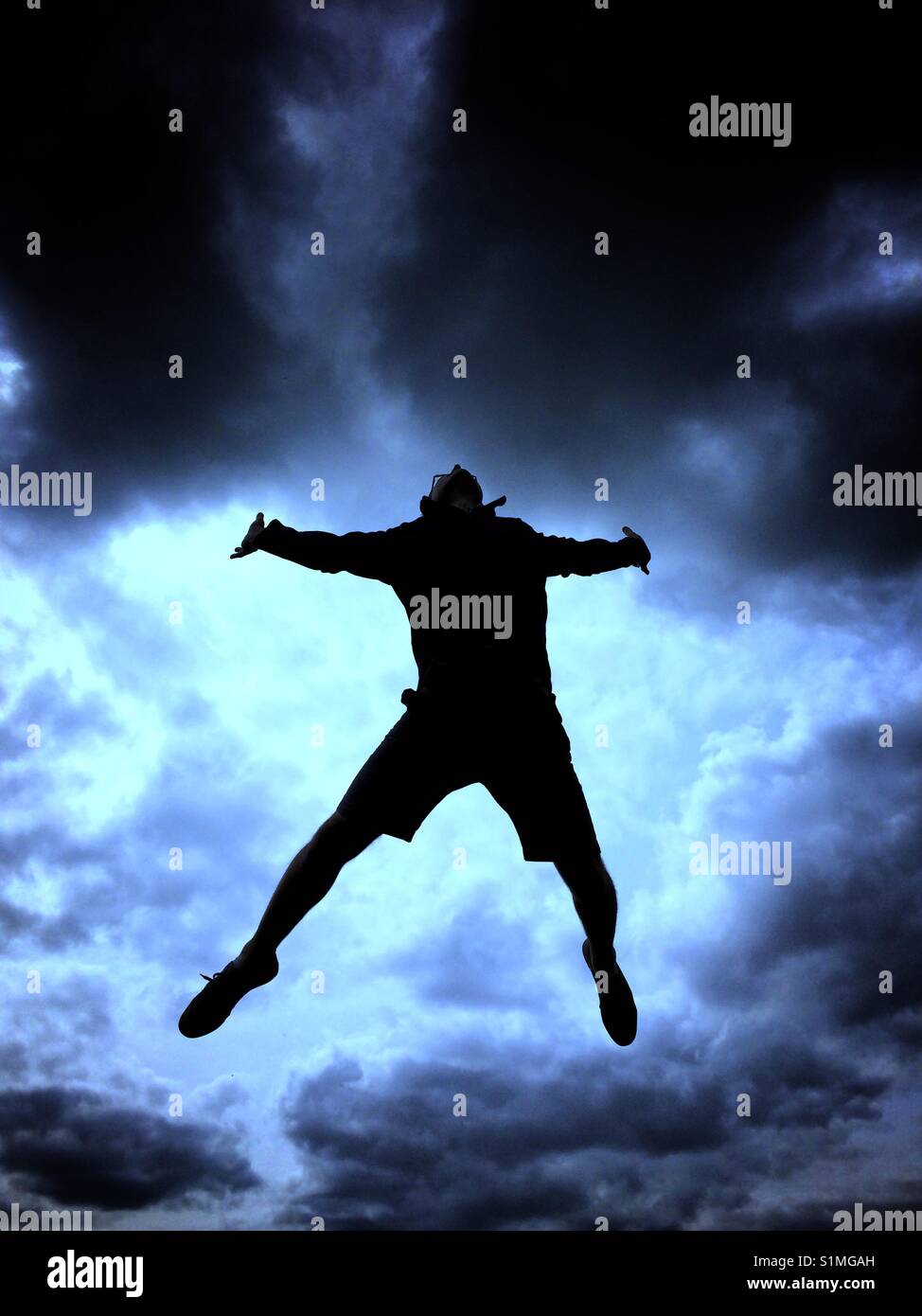La silhouette di un uomo saltare in aria in alto con un blu brillante, elettrico e tempestoso cielo dietro. Foto Stock