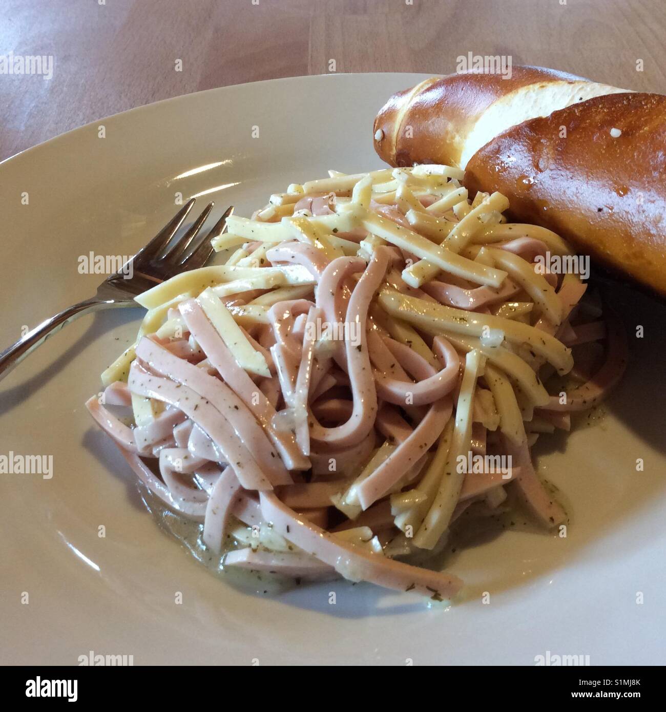 Insalata di fatti in casa fatta di strisce di salsicce e formaggio sulla piastra bianca e pretzel bavarese. Svizzera insalata di salsiccia. Foto Stock