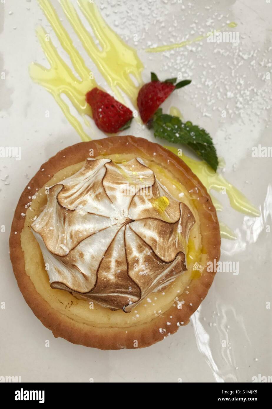 Guardando verso il basso sulla deliziosa Lemon Meringue tart con fragola e menta guarnire sulla piastra bianca spolverato di zucchero a velo - Immagine stock catturata con smartphone