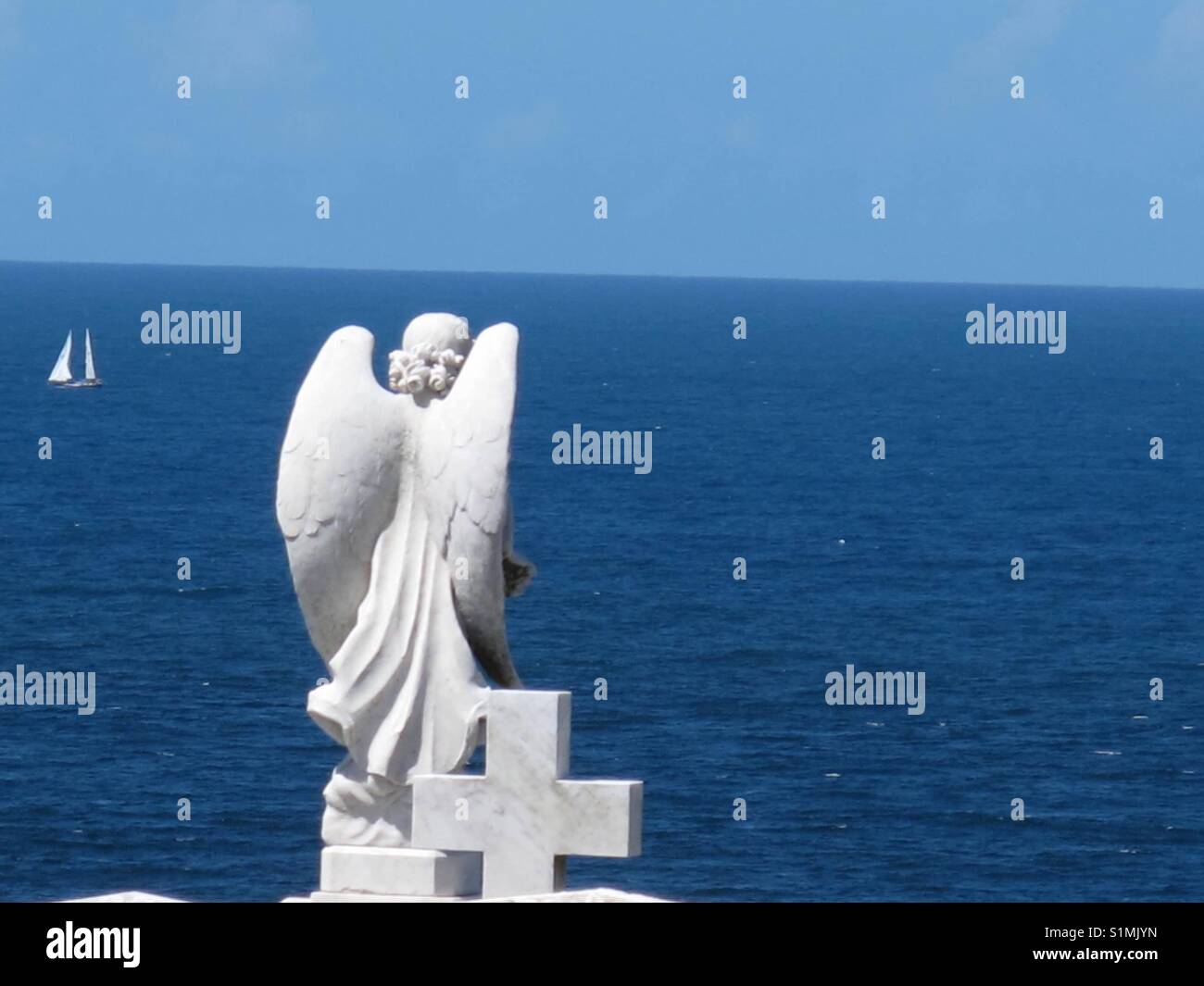 Angelo statua in bianco che si affaccia su un mare blu circondato da un cielo blu.. Foto Stock