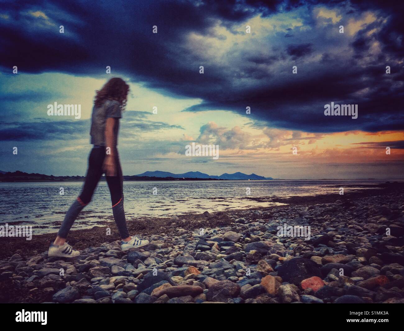 Giovane ragazza camminare sulla spiaggia di ciottoli al tramonto Foto Stock