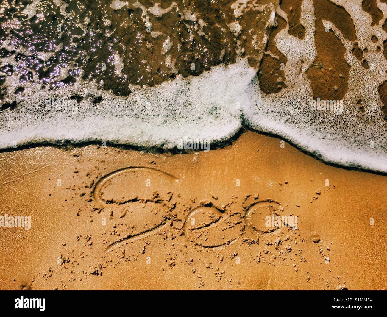 Marea di mare di cancellazione scritte sulla sabbia Foto Stock