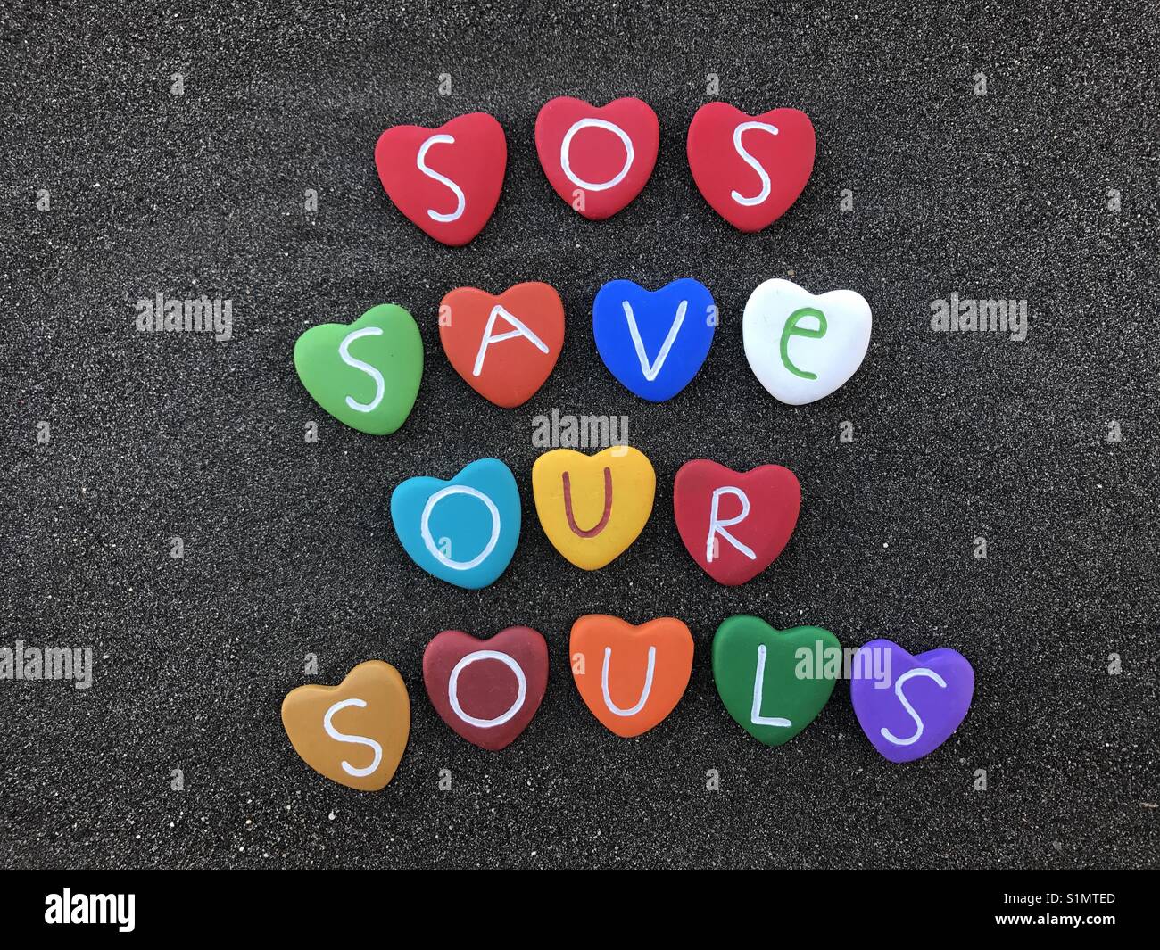 SOS, salva le nostre anime, international codice Morse segnale di emergenza con cuore colorato pietre su sabbia nera vulcanica Foto Stock