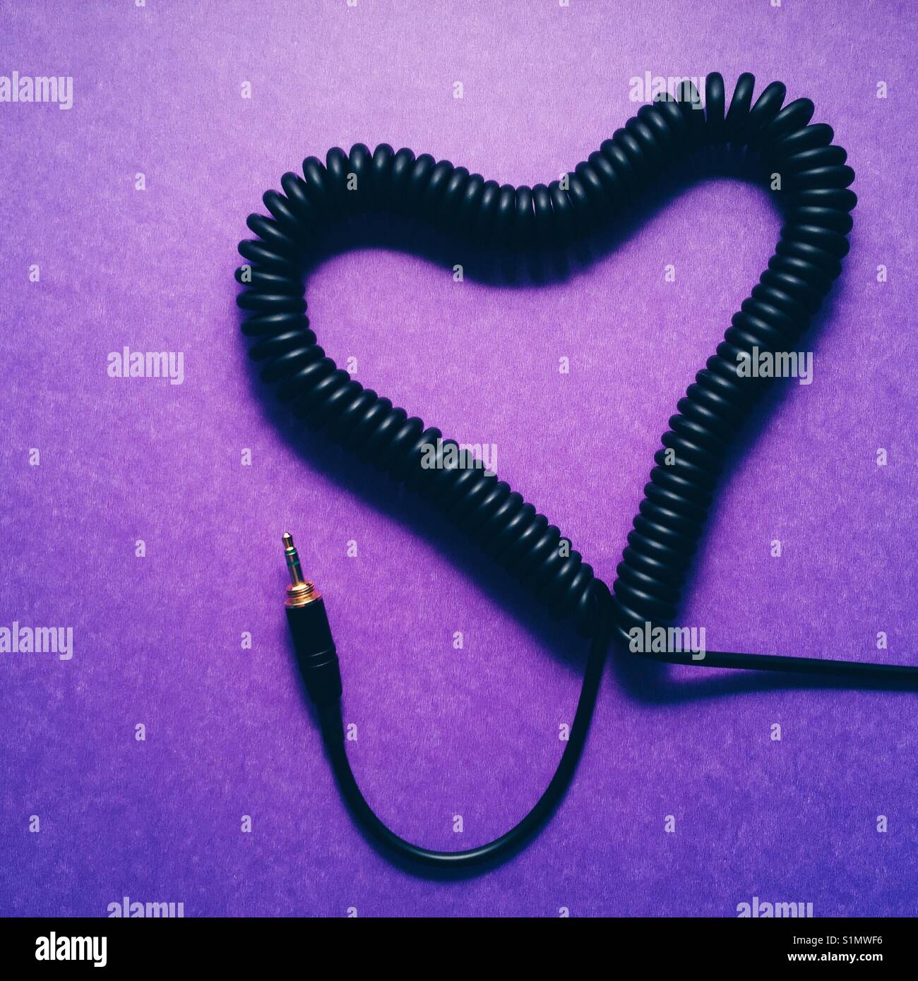 Una spirale cavo cuffia realizzata in una forma di cuore su uno sfondo viola Foto Stock