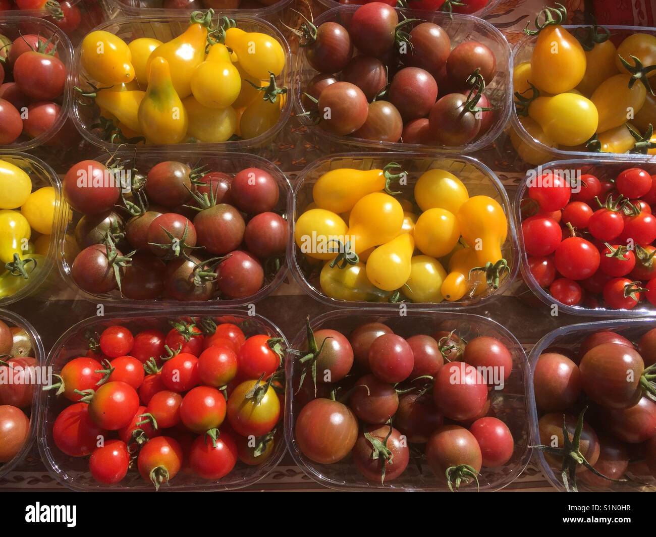 Punnets contenente diverse varietà di rosso, giallo e arancione di pomodori ciliegini in vendita su un mercato in stallo. Foto Stock