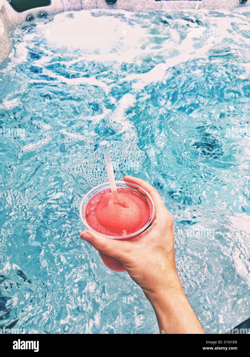 Slush drink di ghiaccio in una mano mentre è seduto in una jacuzzi esterna - Immagine stock catturata con smartphone
