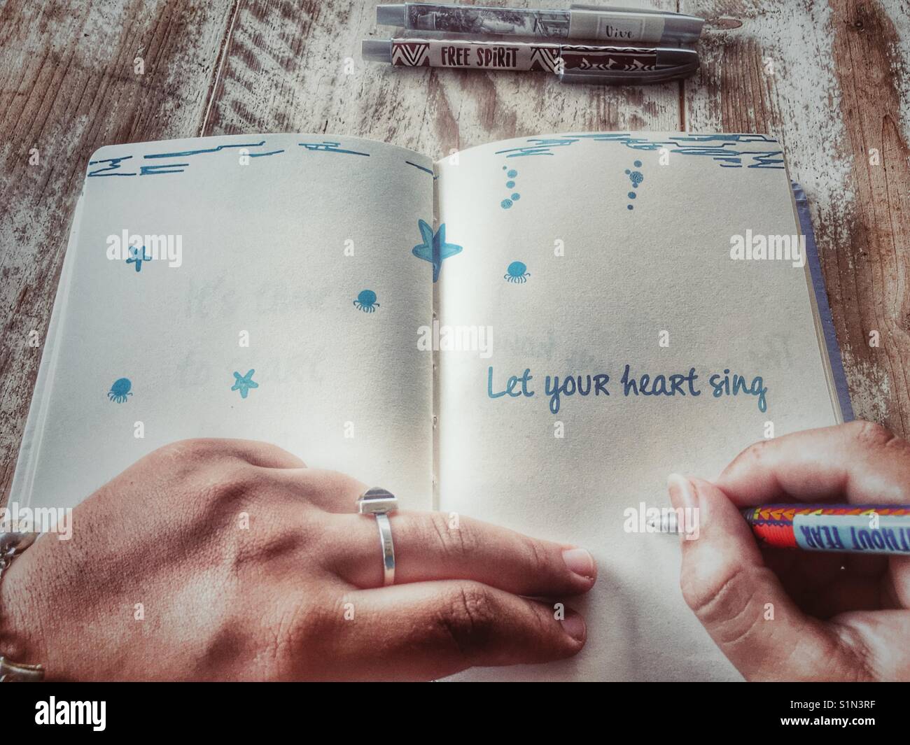 Donna che mantiene una penna per scrivere in un ufficiale con il mantra lasciate che il vostro cuore cantare stampata sulla pagina Foto Stock