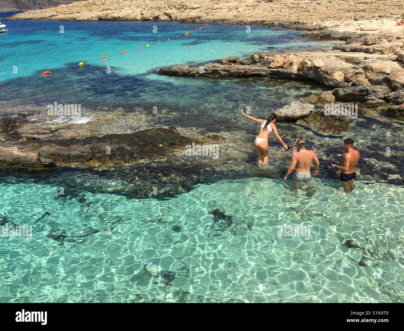 I turisti in acque calde e cristalline ingresso nella insenatura di sabbia su Comino e Malta Foto Stock