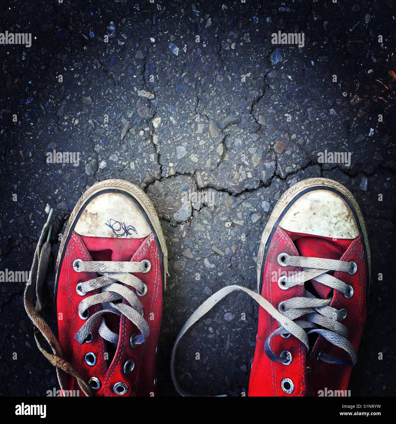 Un vecchio usurato coppia di tela rossa sneakers su un manto di asfalto Foto Stock