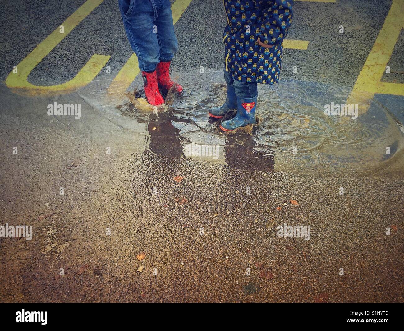 I due ragazzi in stivali da pioggia di saltare in una pozzanghera Foto Stock