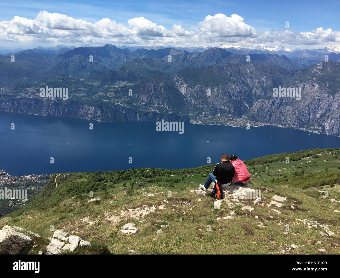 Due persone sedersi sul Monte Baldo, Italia guardando in giù sul Lago di Garda, con la città di Limone in background Foto Stock