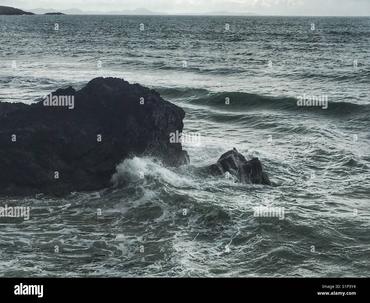Onde e spruzzi di schiantarsi intorno a Lion Rock, rhosneigr, Anglesey, Galles del nord Foto Stock