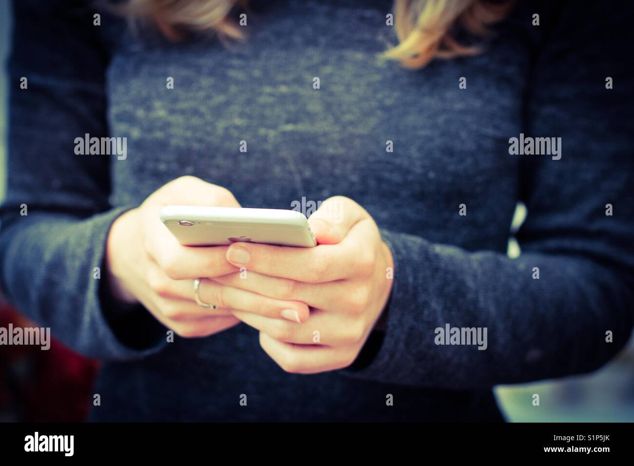 Una sezione mediana di una giovane ragazza in un colore scuro abito in possesso di un telefono cellulare nelle sue mani mentre scrivere un messaggio Foto Stock