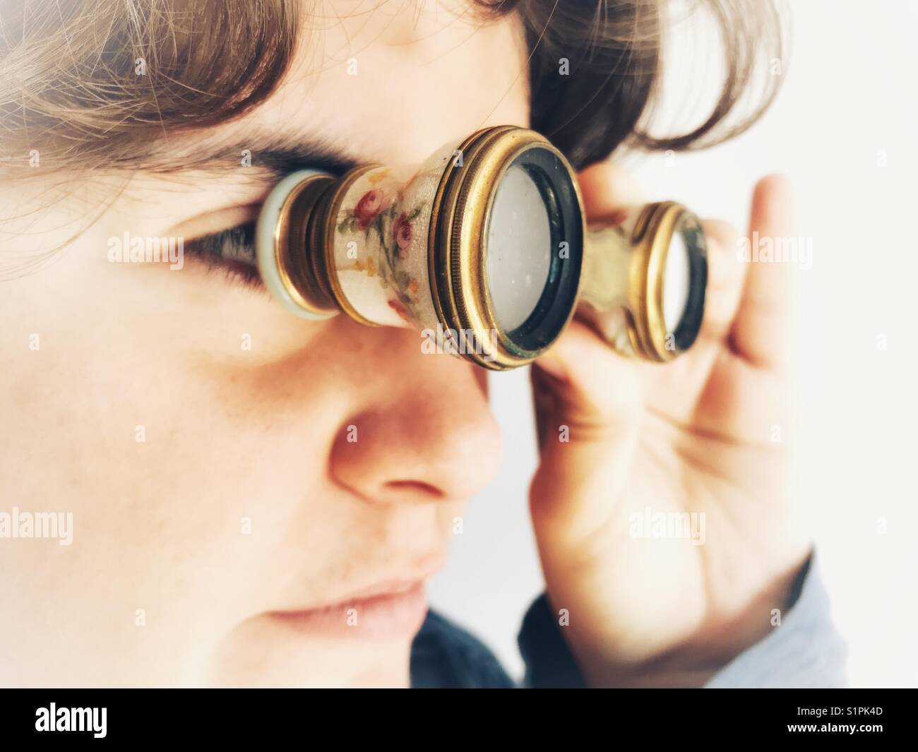La millenaria donna guardando attraverso un paio di occhiali di opera, vecchio stile binocoli per uso a teatro e opera Foto Stock