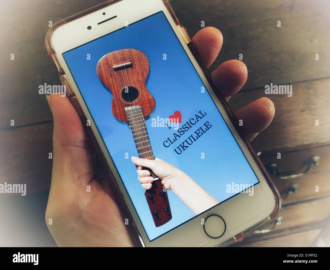 IPhone in mano, con i ❤️ Ukulele classica foto di sfondo sullo schermo. (Lo sfondo è la mia immagine e design). Foto Stock