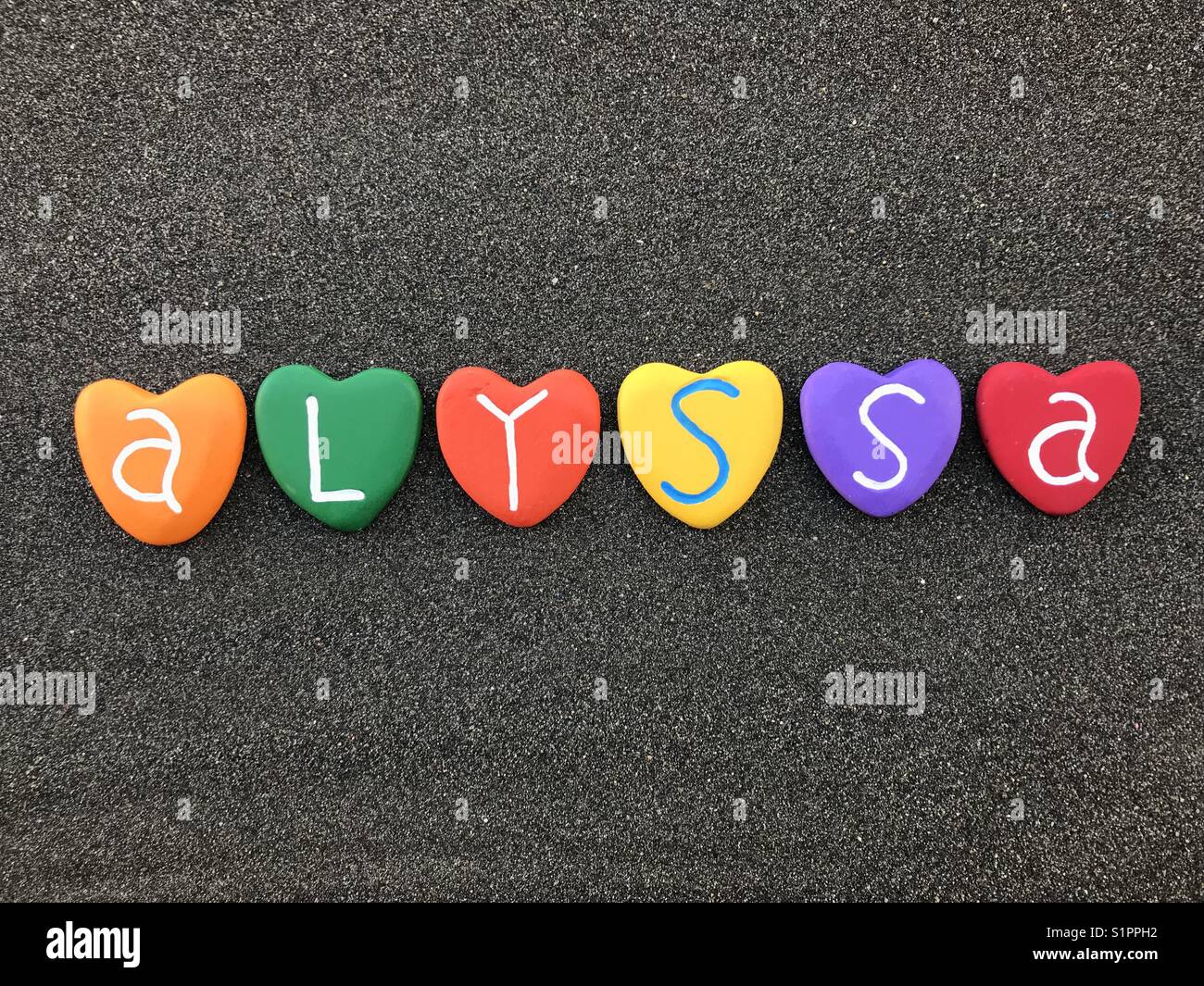 Alyssa, nome femminile con cuore colorato pietre su sabbia nera vulcanica Foto Stock