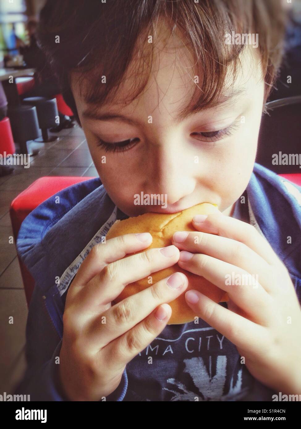 Un ragazzo che prende un morso da un hamburger. - Immagine stock catturata con smartphone
