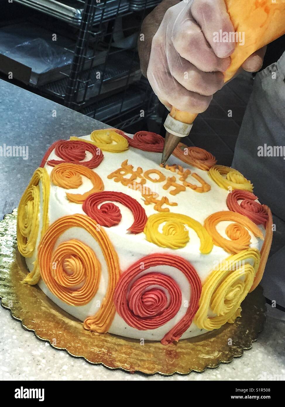 Un uomo scrive su un colorato torta di compleanno con ciliegina Foto Stock
