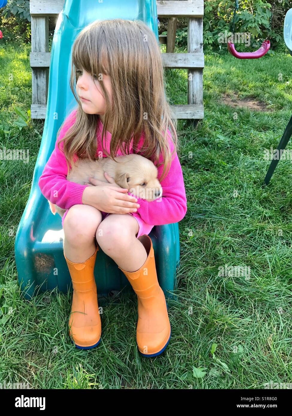 Ragazza giovane indossando orange wellies tenendo un cucciolo Foto Stock