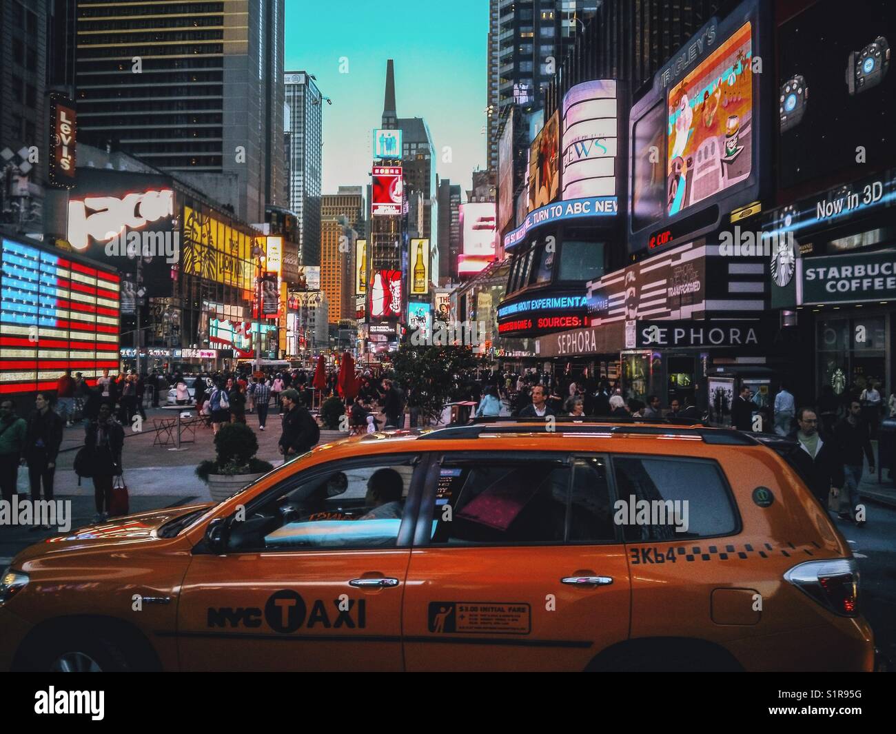 Yellow taxi passando da una trafficata Time Square in prima serata Foto Stock