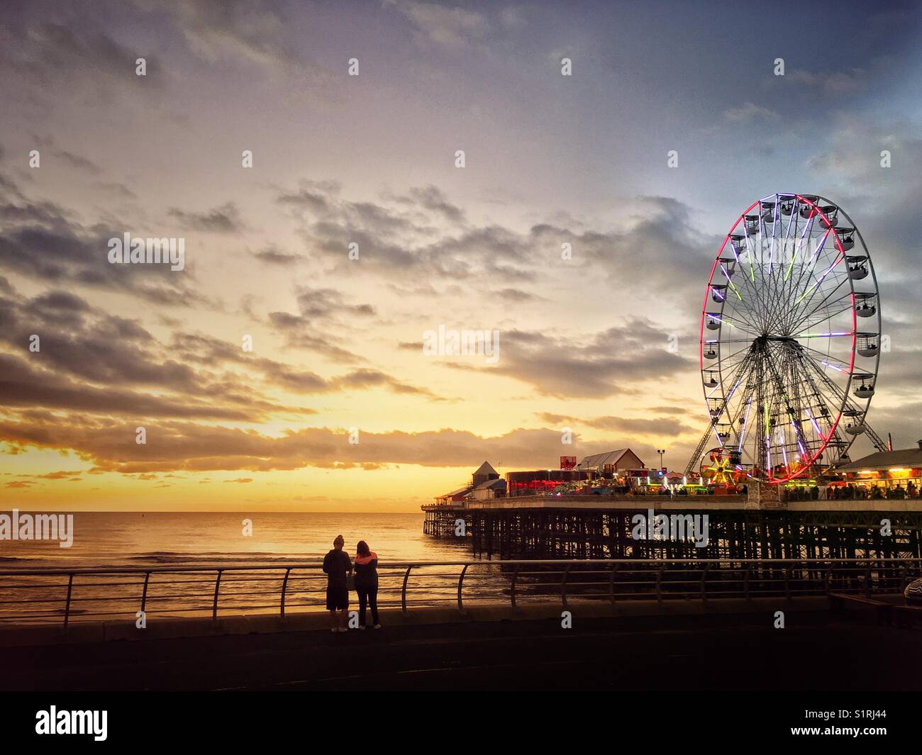 Due persone a guardare il tramonto dal accanto alla centrale illuminata Pier di Blackpool Foto Stock