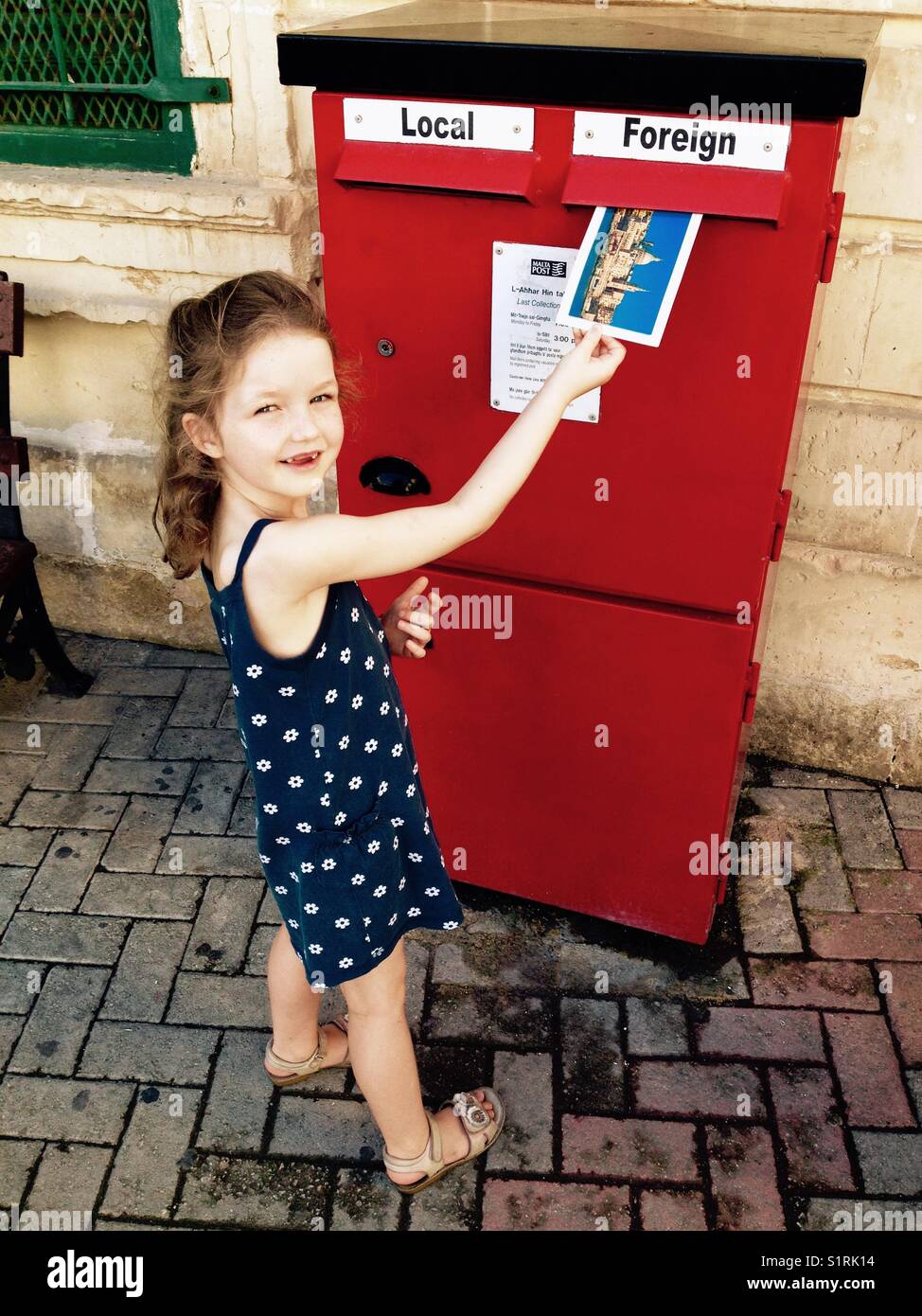 Giovane ragazza / bambino / bambino posti la sua cartolina in una buca delle lettere / red letter box / Casella di posta elettronica attraverso lo slot contrassegnato posta estera. Malta. Foto Stock