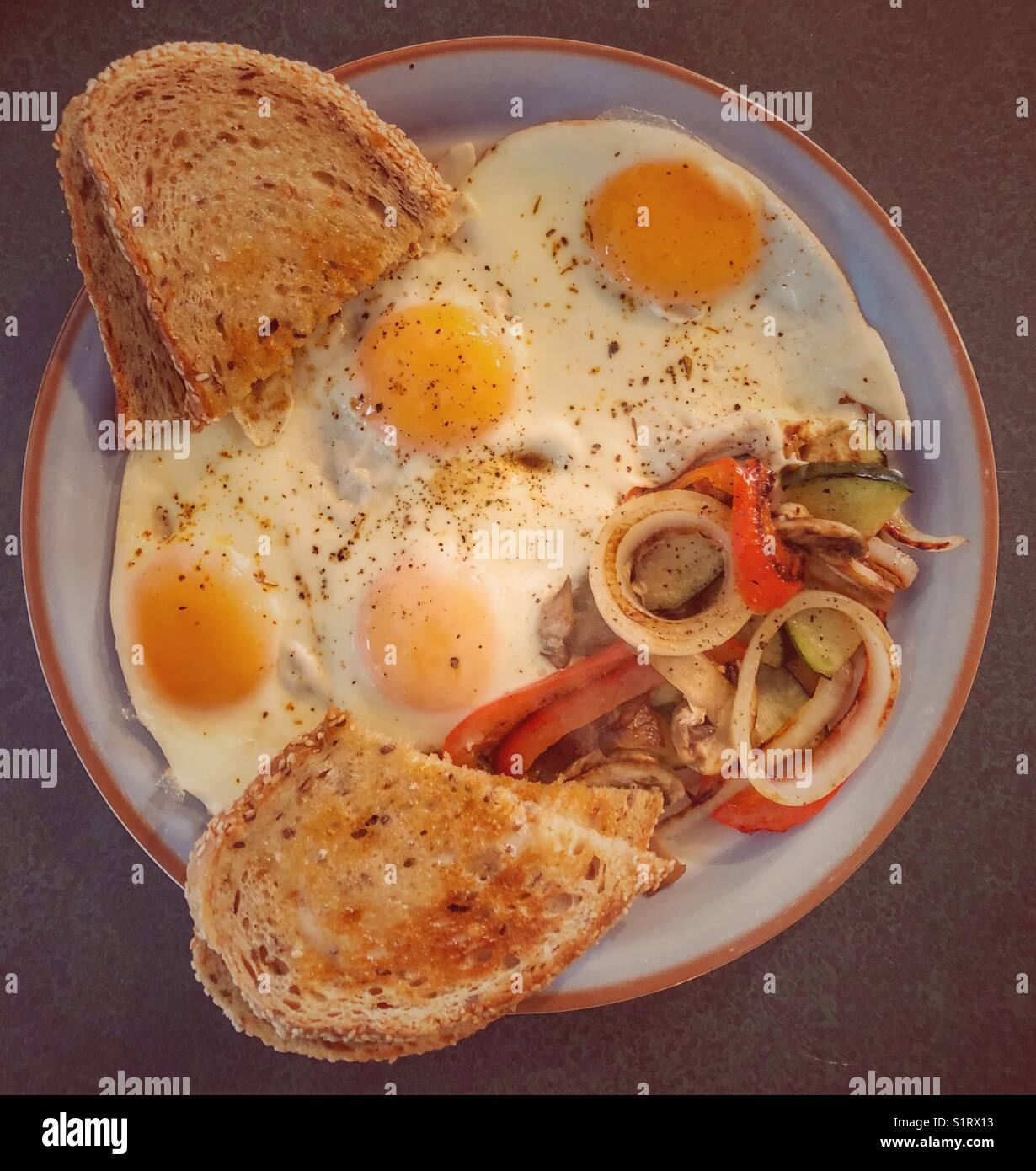 Vista piatta di quattro uova con la parte soleggiata in alto con cipolla alla griglia, zucchine, funghi, peperoni rossi e toast multigrain Foto Stock