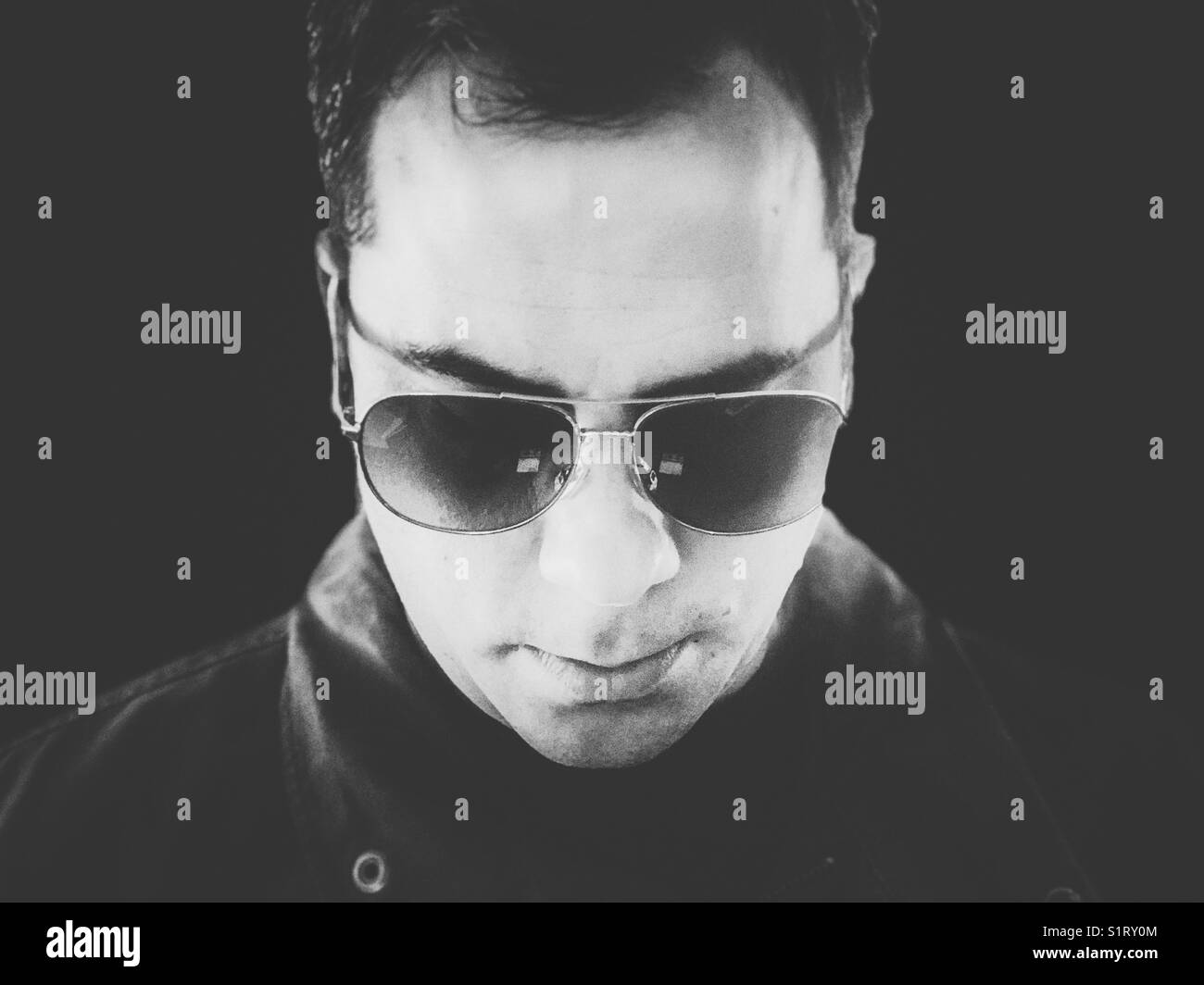 Immagine in bianco e nero di un uomo che indossa occhiali da sole aviatore che guarda in basso - Immagine stock catturata con smartphone