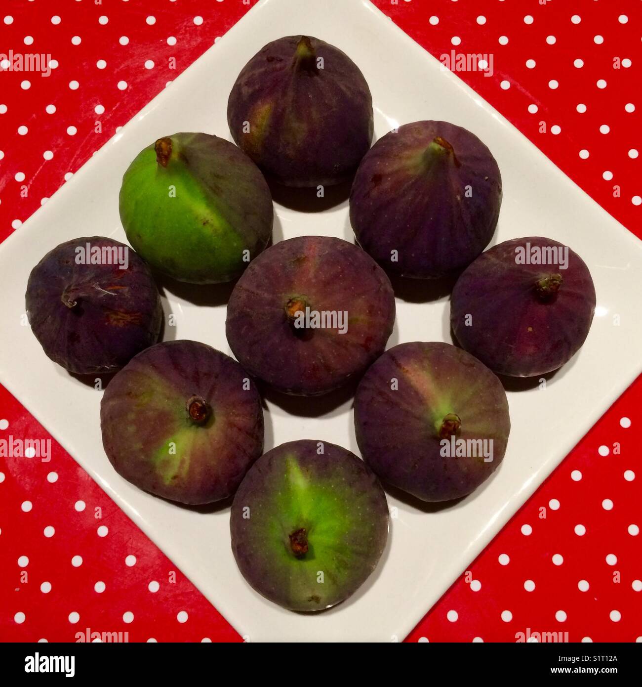 Una serie di 9 fichi freschi su un piatto bianco su un tappetino rosso con punti bianchi. - Immagine stock catturata con smartphone