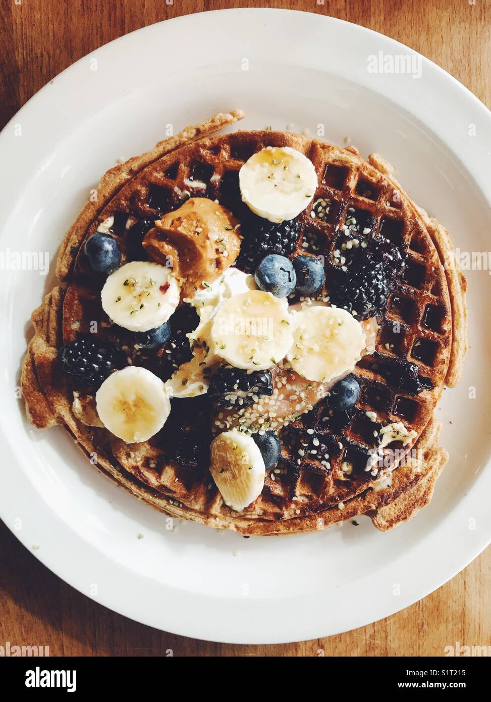 Waffle a colazione. Vista dall'alto di un waffle con banana, mirtilli, more, burro di arachidi, panna acida e semi di canapa. - Immagine stock catturata con smartphone