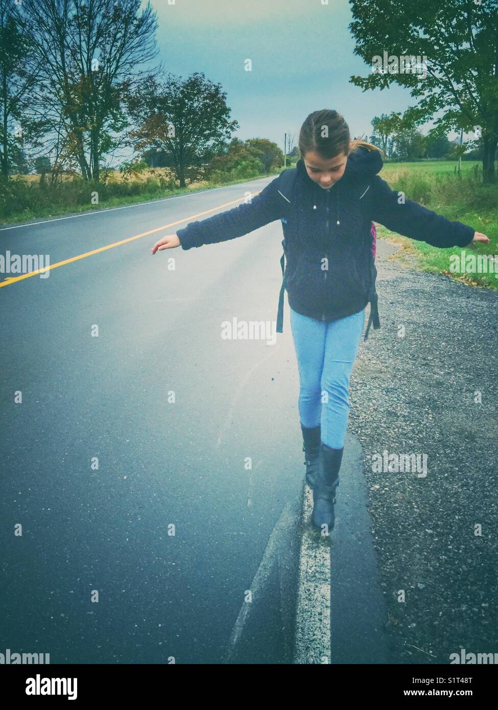 Ragazza che cammina sulla linea dipinta lungo il lato della strada nel sud dell'Ontario, Canada Foto Stock