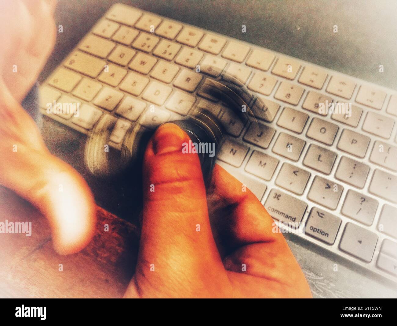 Millennial che gioca con un Fidget Spinner, mentre si siede su una scrivania rivestita in pelle con una tastiera wireless per computer - Immagine stock catturata con smartphone