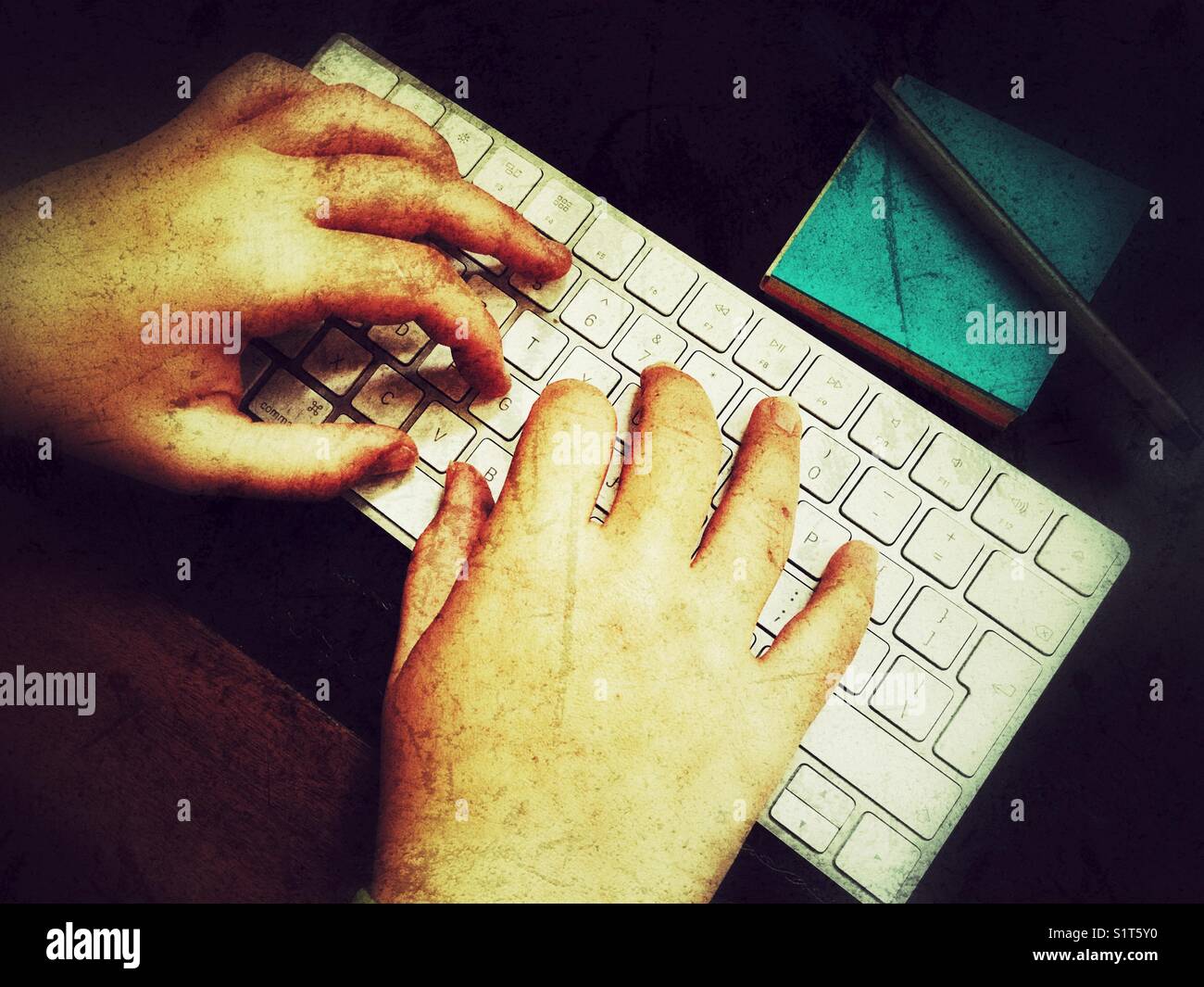 Le mani della donna Millennial sulla tastiera del computer con una penna su un blocco note blu. Foto Stock