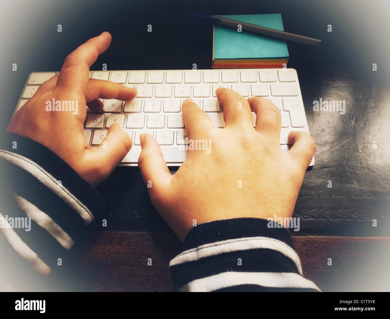 Le mani della donna Millennial sulla tastiera del computer con una penna su un blocco note blu. Foto Stock