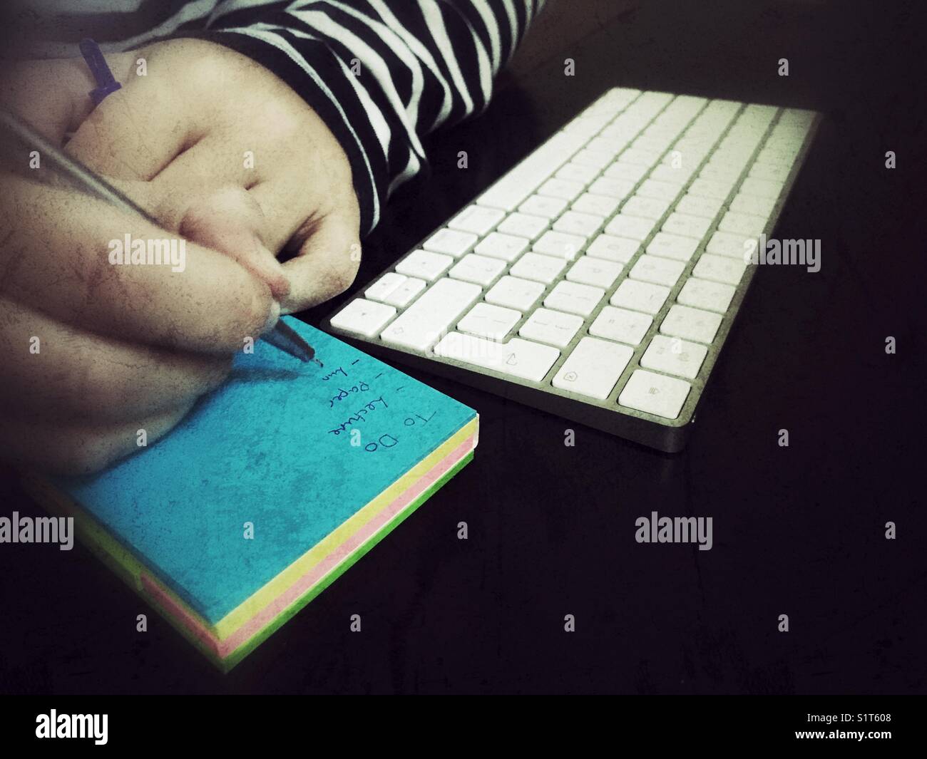 Donna millenaria che fa un elenco su un blocco note, con tastiera per computer su desktop. - Immagine stock catturata con smartphone