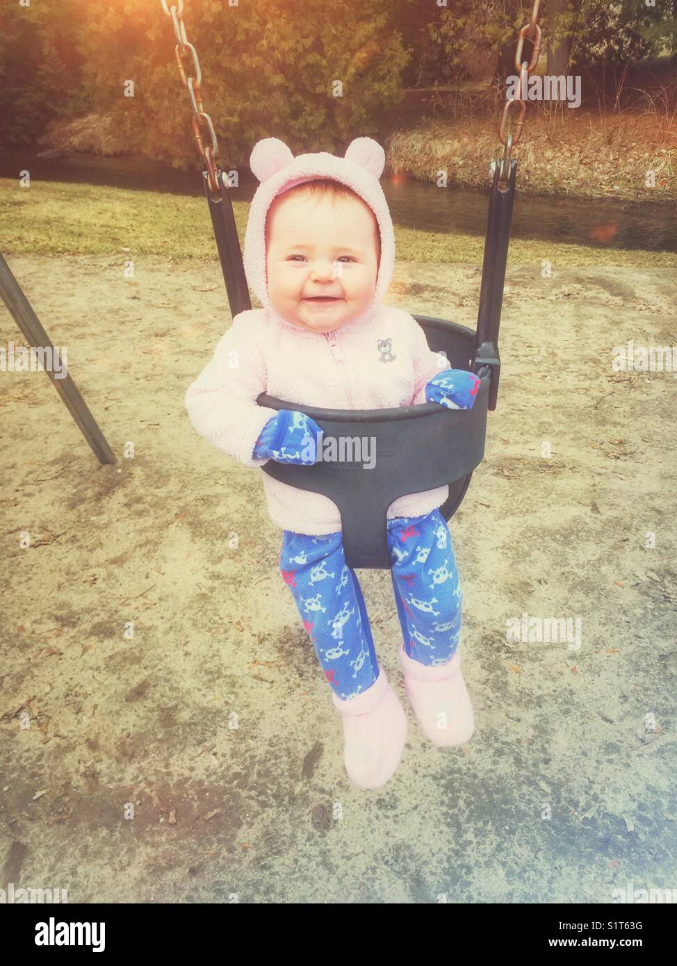 Bambina sorridente e felice in un'altalena infantile in un parco Foto Stock