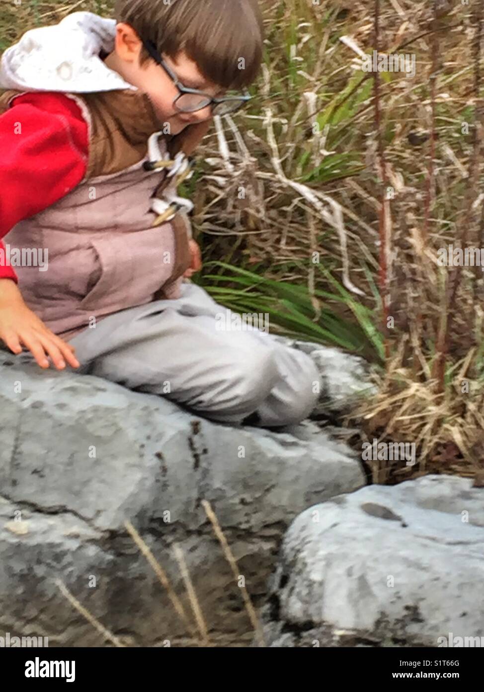 Bambino in ambiente naturale, seduto su di una roccia. Foto Stock