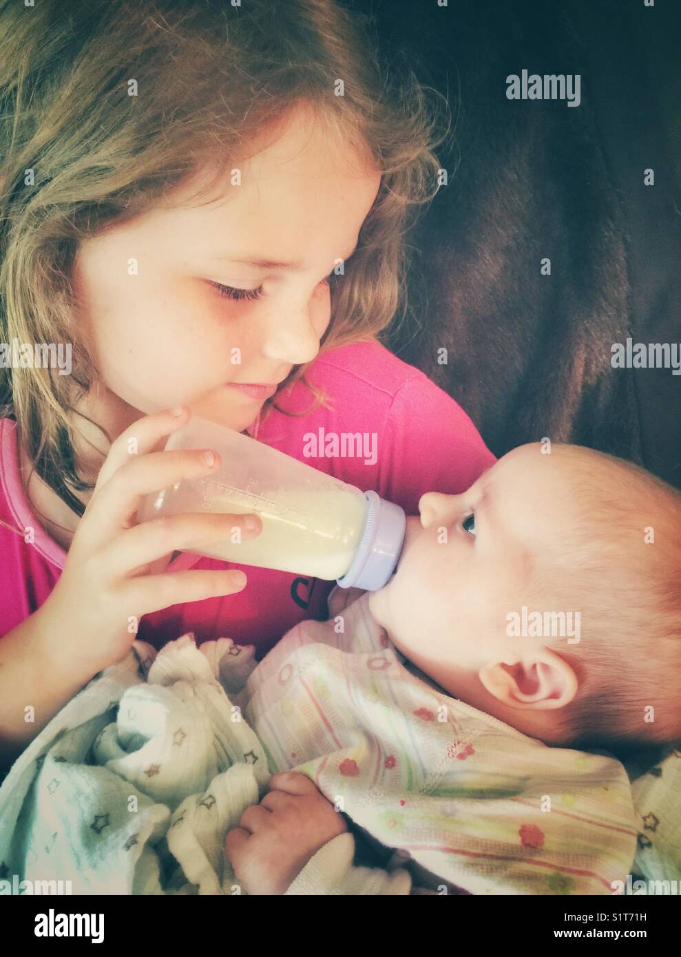 La sorella maggiore alimentazione di baby sorella una bottiglia di latte  materno Foto stock - Alamy