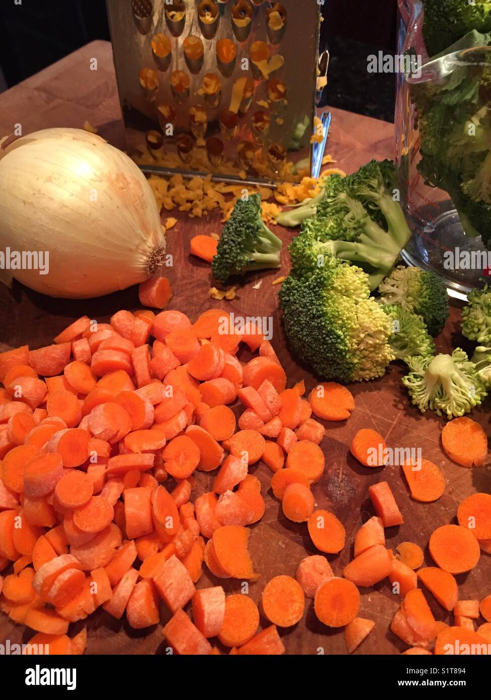 Ortaggi freschi compresi green broccoli, carote arancione e giallo cipolla con formaggio Cheddar grattugiato sono seduti sul tagliere di legno pronti per essere cucinati. Foto Stock