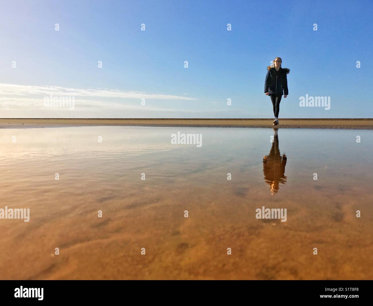 Una giovane ragazza sola sulla spiaggia si riflette in una piscina d'acqua con la bassa marea Foto Stock