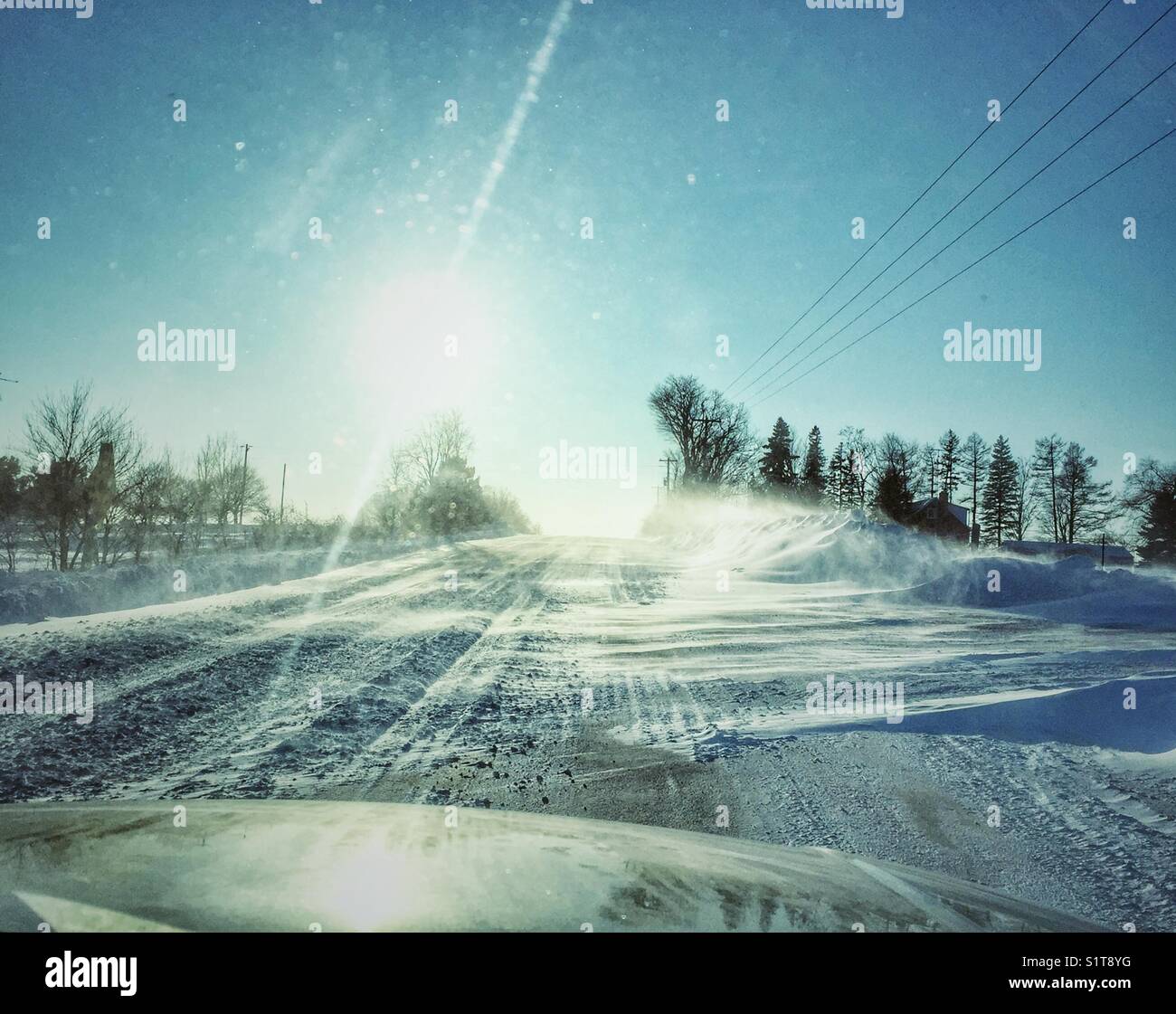 Rifiuti pericolosi guida invernale nelle zone rurali di Ontario, Canada con raffiche di neve sulla strada e sole accecante Foto Stock