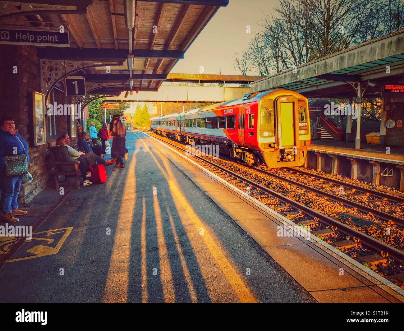 Le persone e le ombre sul rail station piattaforma con un treno in avvicinamento. Sherborne, Dorset, Inghilterra Foto Stock