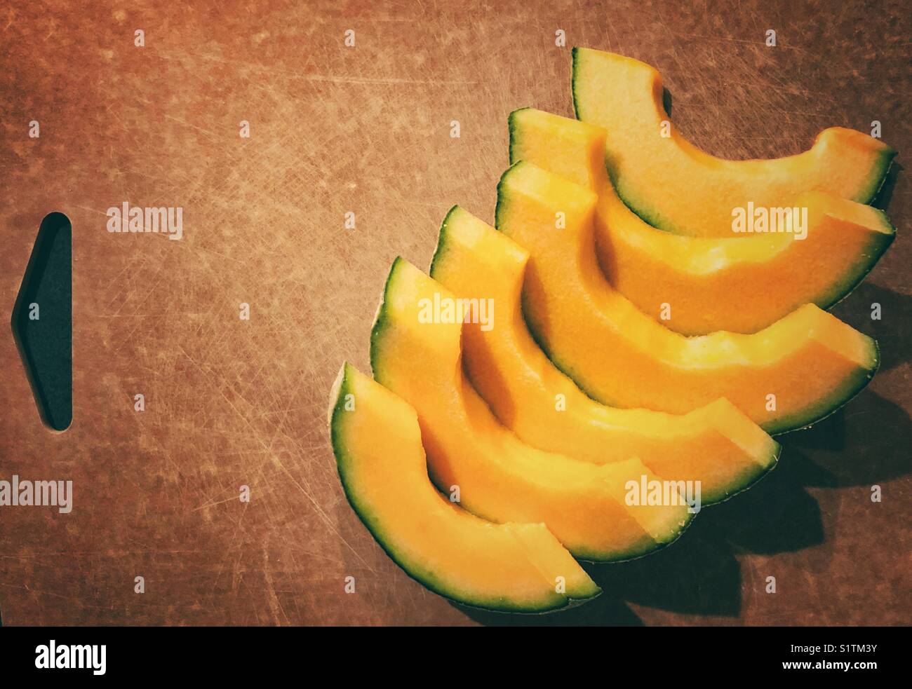Fette di melone cantaloupe ben disposte su un tagliere marrone Foto Stock