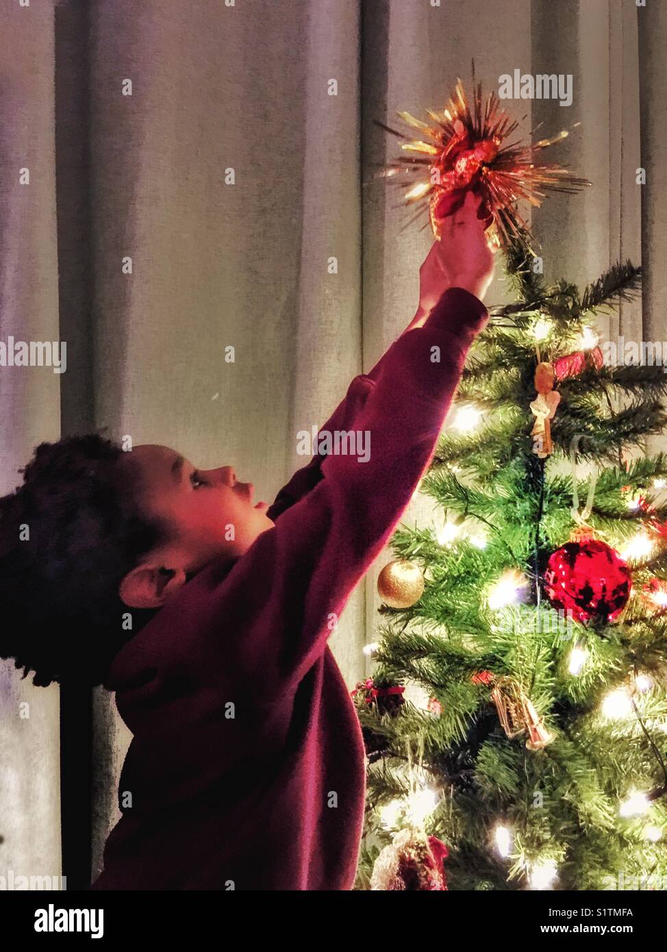 Un ragazzino raggiunge fino a decorare un albero di natale. Foto Stock