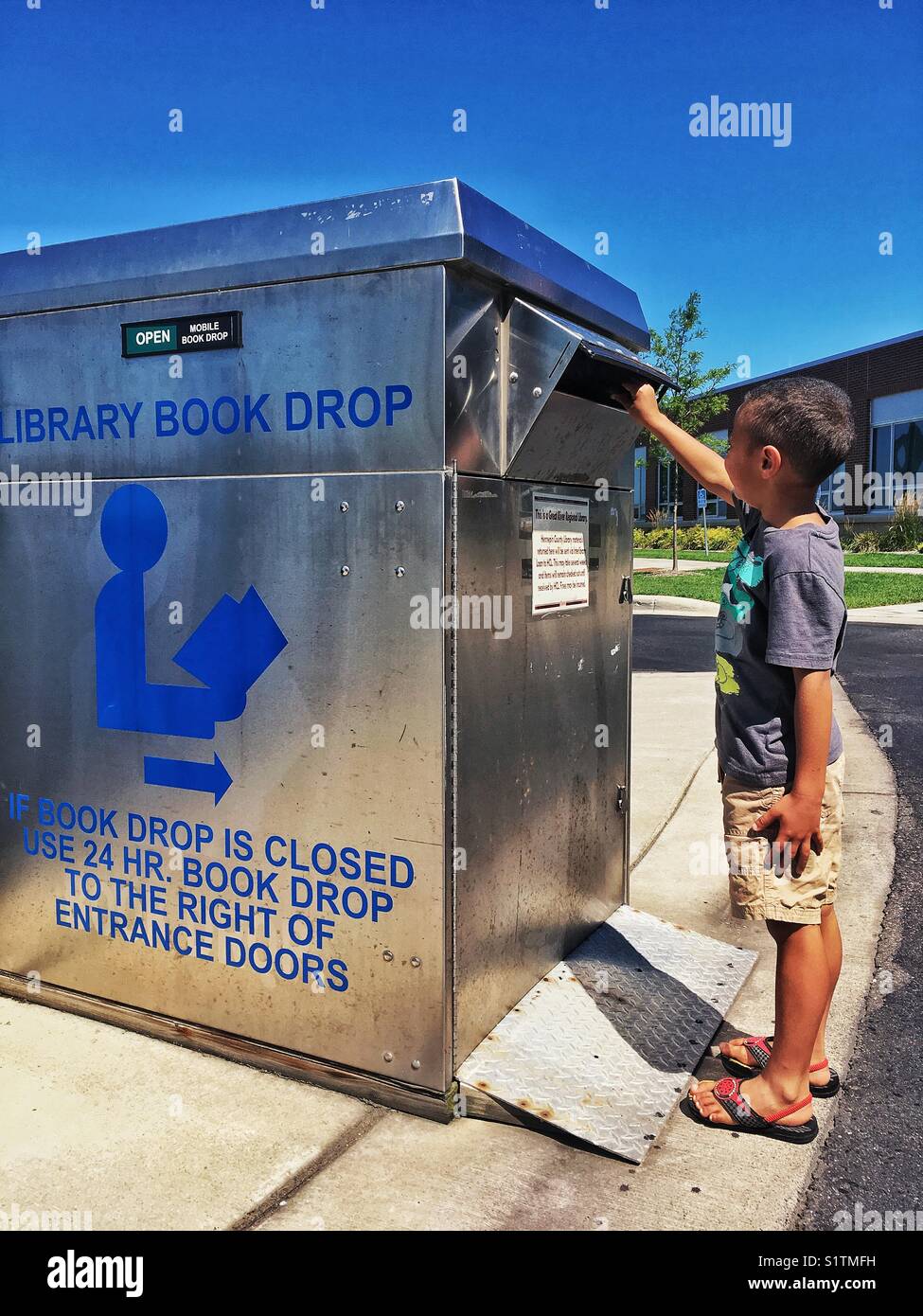 Ragazzo afro-americana da un libro della biblioteca drop box di restituire un libro. Foto Stock