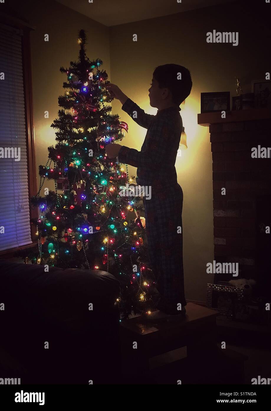 Little Boy in piedi su uno sgabello per aiutare a decorare albero di natale Foto Stock